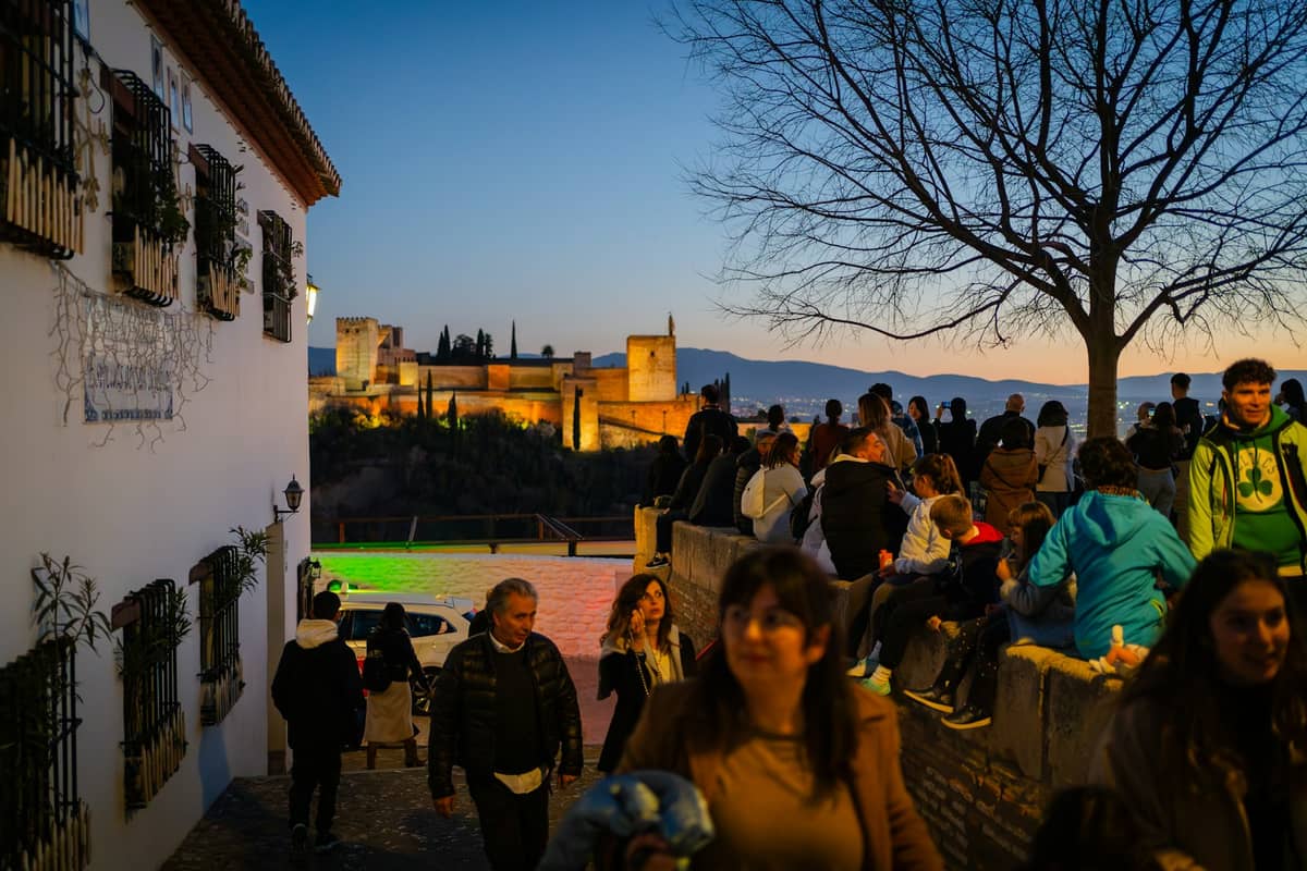 ฝูงชนมารวมตัวกันยามพลบค่ำที่จุดชมวิว Mirador de San Nicolás พร้อมชมทัศนียภาพอันสวยงามของ Alhambra และ Sierra Nevada ในระยะไกล