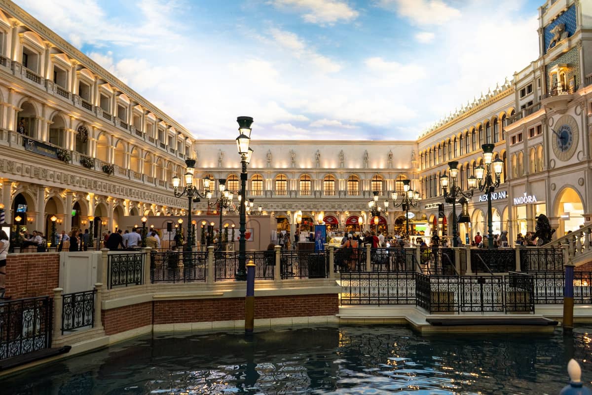 Zona comercial interior de The Venetian en Las Vegas con cielo artificial, arquitectura clásica, canal y personas de turismo y compras.