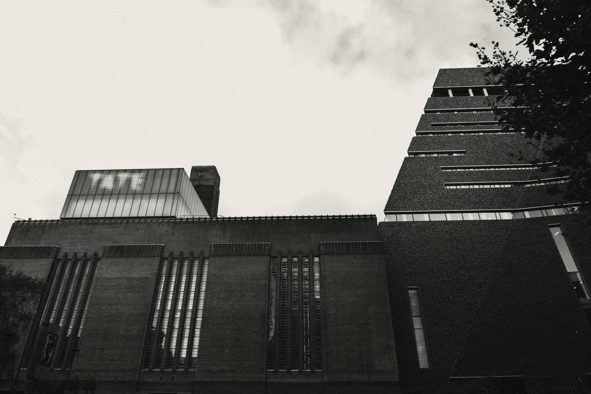 Foto em preto e branco do exterior do Tate Modern em Londres, com a inscrição TATE visível no edifício.