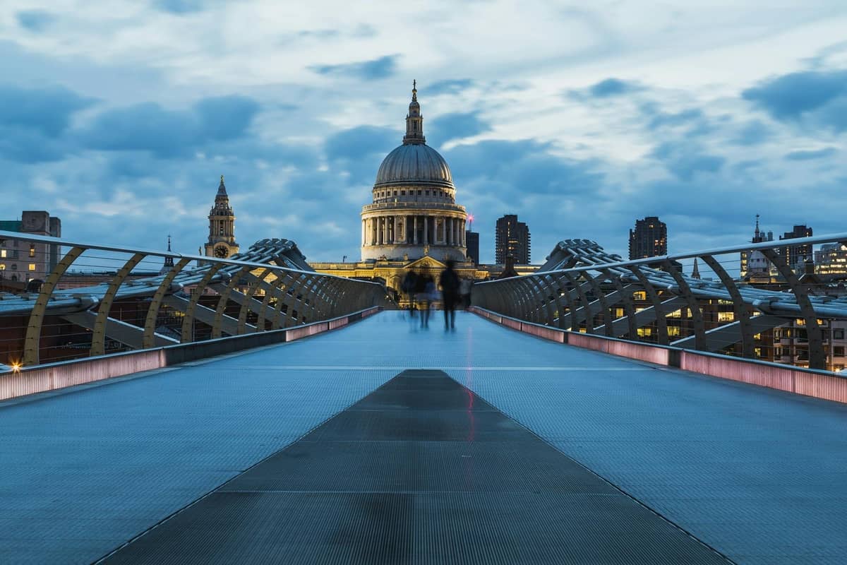 Vista a partir da Millennium Bridge em direção à Catedral de St. Paul's ao entardecer, com céus dramáticos e o horizonte de Londres ao fundo.