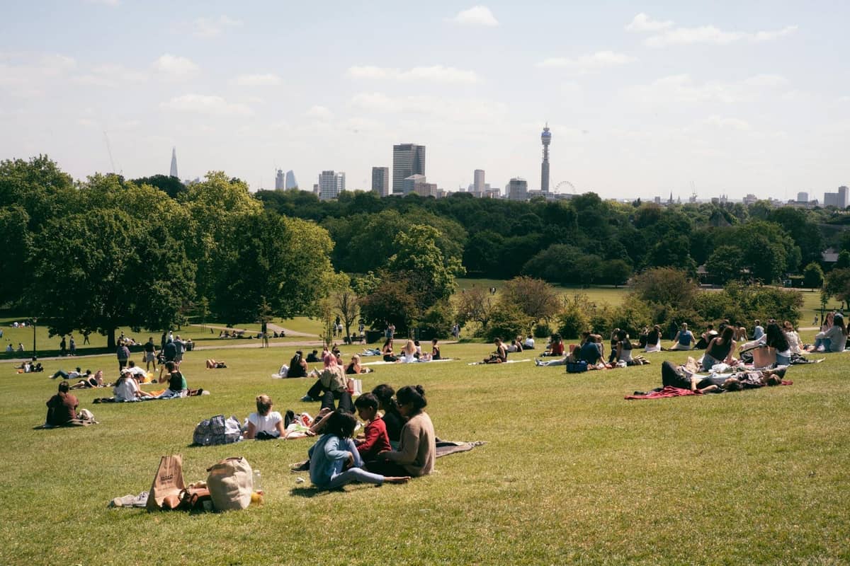 Pessoas relaxando em uma colina gramada em um parque com uma vista clara do horizonte de Londres, incluindo a BT Tower.