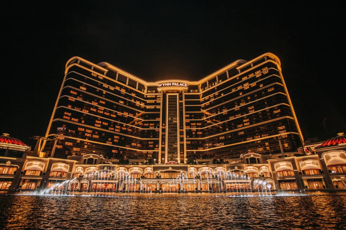 Nächtliche Ansicht des Wynn Palace Macau mit beleuchtetem Gebäudeäußeren und Springbrunnendarbietung davor.