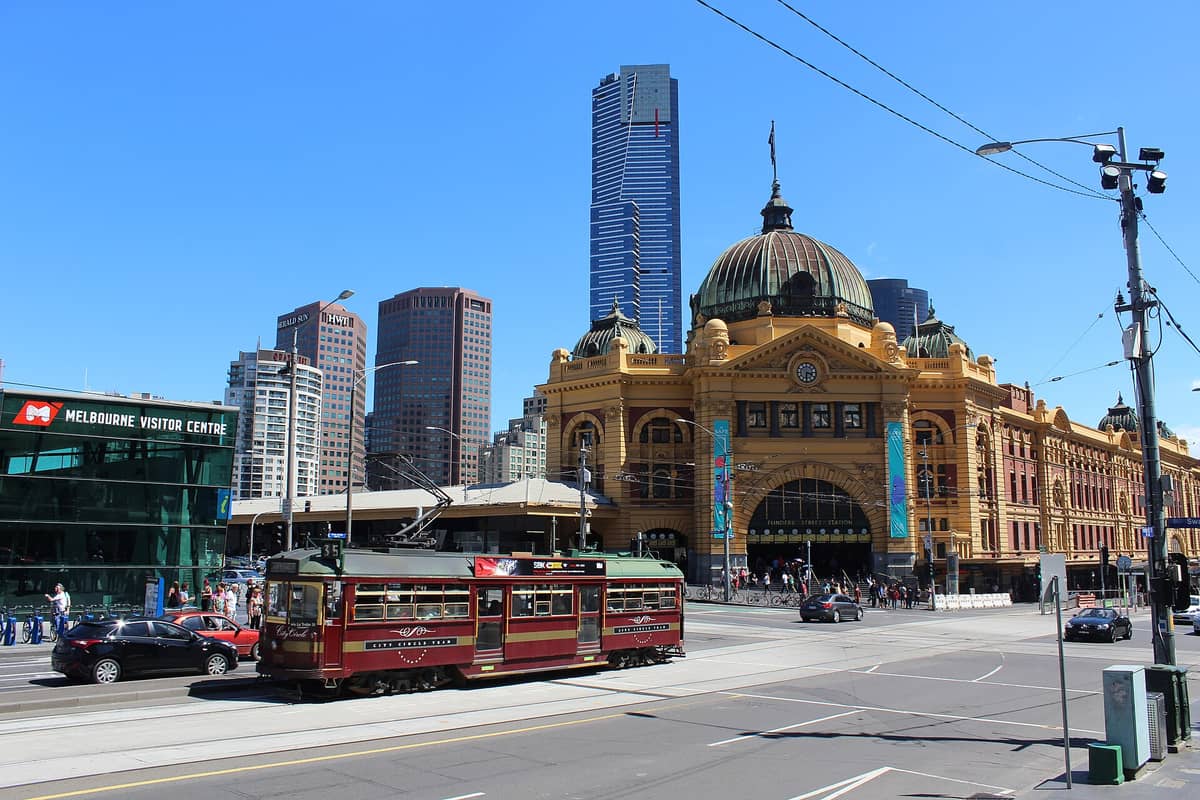 Vue de jour de la Flinders Street Station de Melbourne avec un tramway City Circle passant devant, des bâtiments modernes en arrière-plan et le Melbourne Visitor Centre visible.