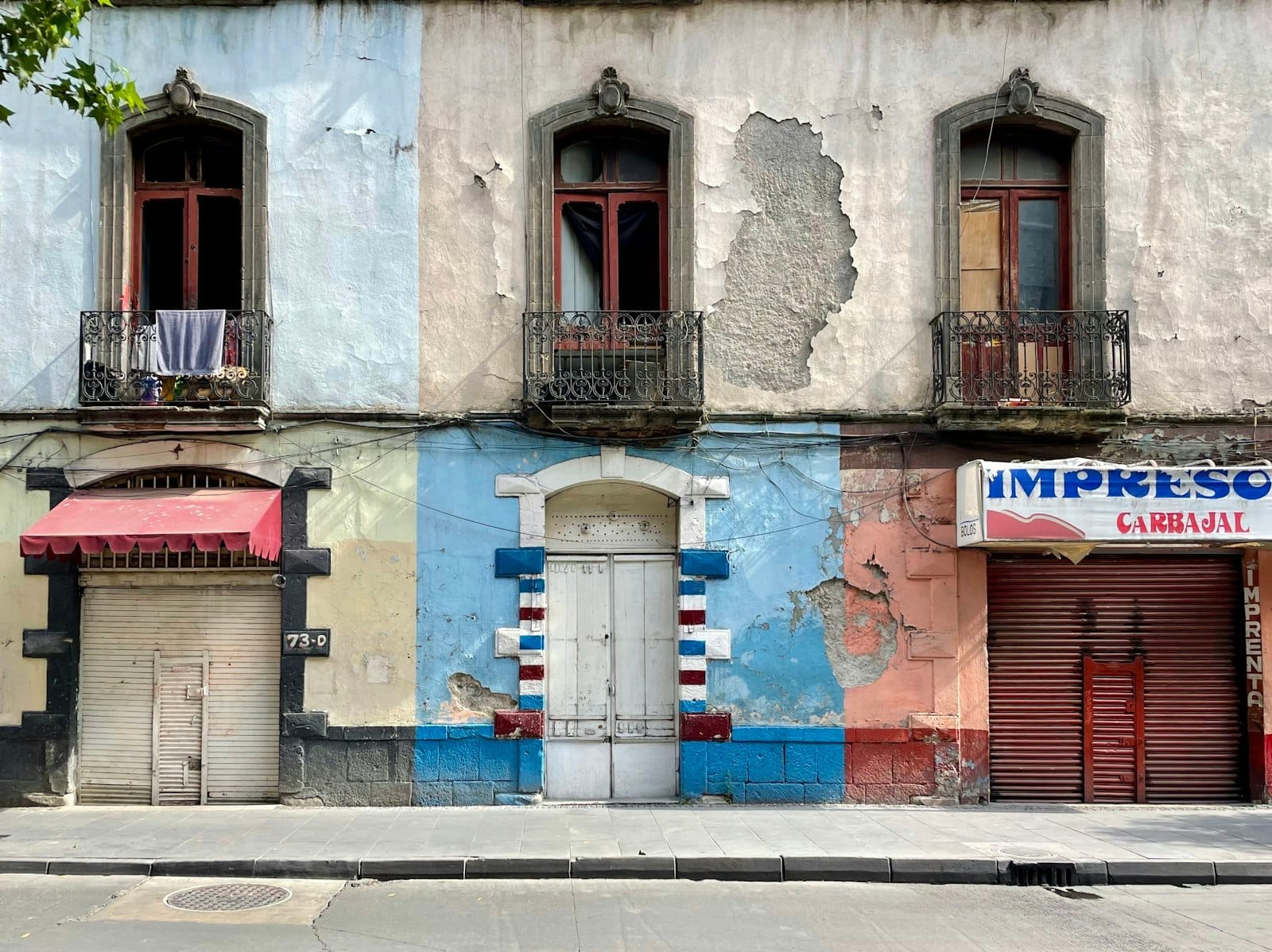Edifício colonial colorido e envelhecido com sacadas e frentes de lojas fechadas em uma rua tranquila da Cidade do México.