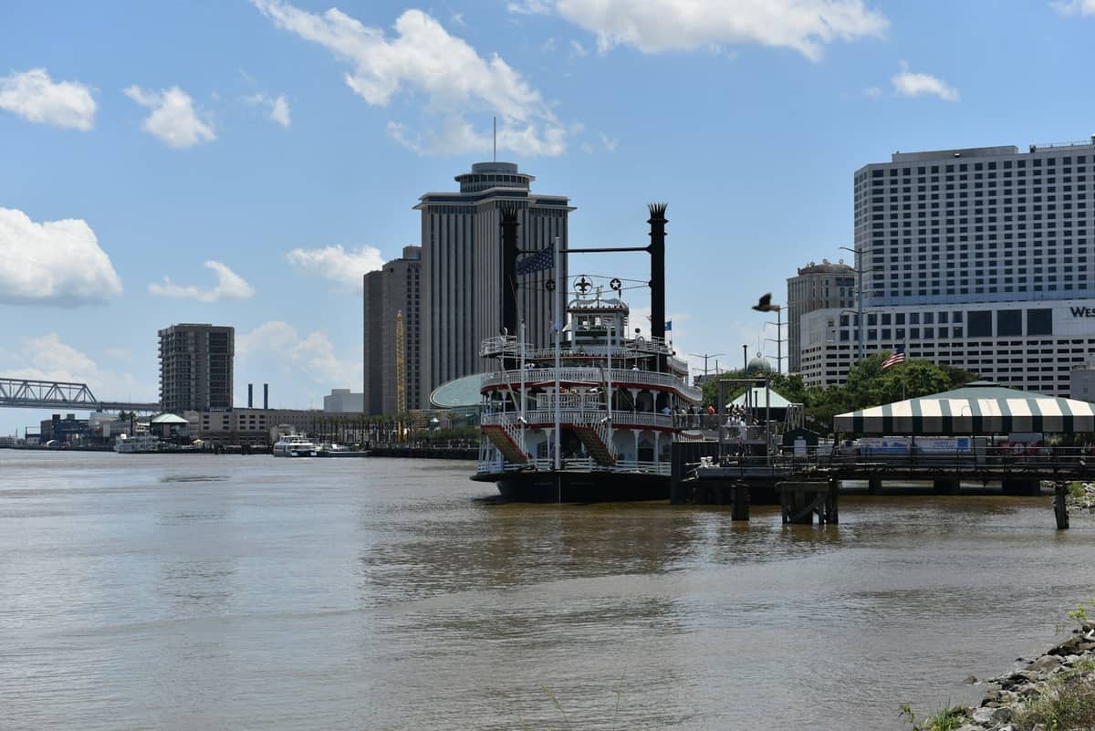 Am Mississippi angedockter Raddampfer mit der Skyline von New Orleans und dem Flussufer an einem hellen Tag.