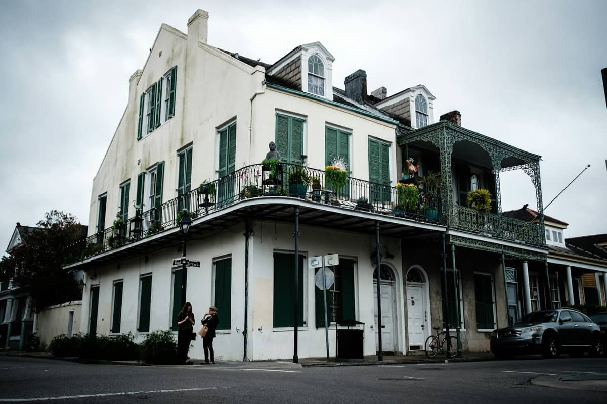 Straßenecke in New Orleans mit einem klassischen Gebäude im French Quarter, das einen schmiedeeisernen Balkon, grüne Fensterläden und darunter spazierengehende Menschen zeigt.