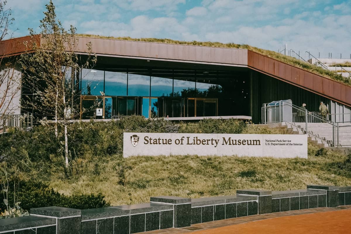 Der Außeneingang des Statue of Liberty Museums mit seinem Schild und moderner Glasfassade, umgeben von Grünflächen.