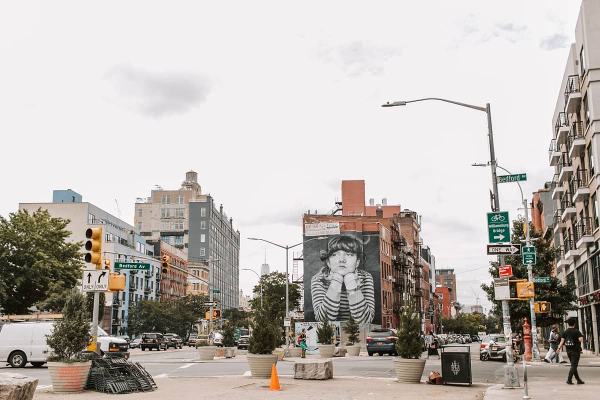 Eine Straßenszene in New York City mit Gebäuden, Straßenschildern, Autos und einem großen Wandbild eines Kindes auf einer Backsteinmauer.