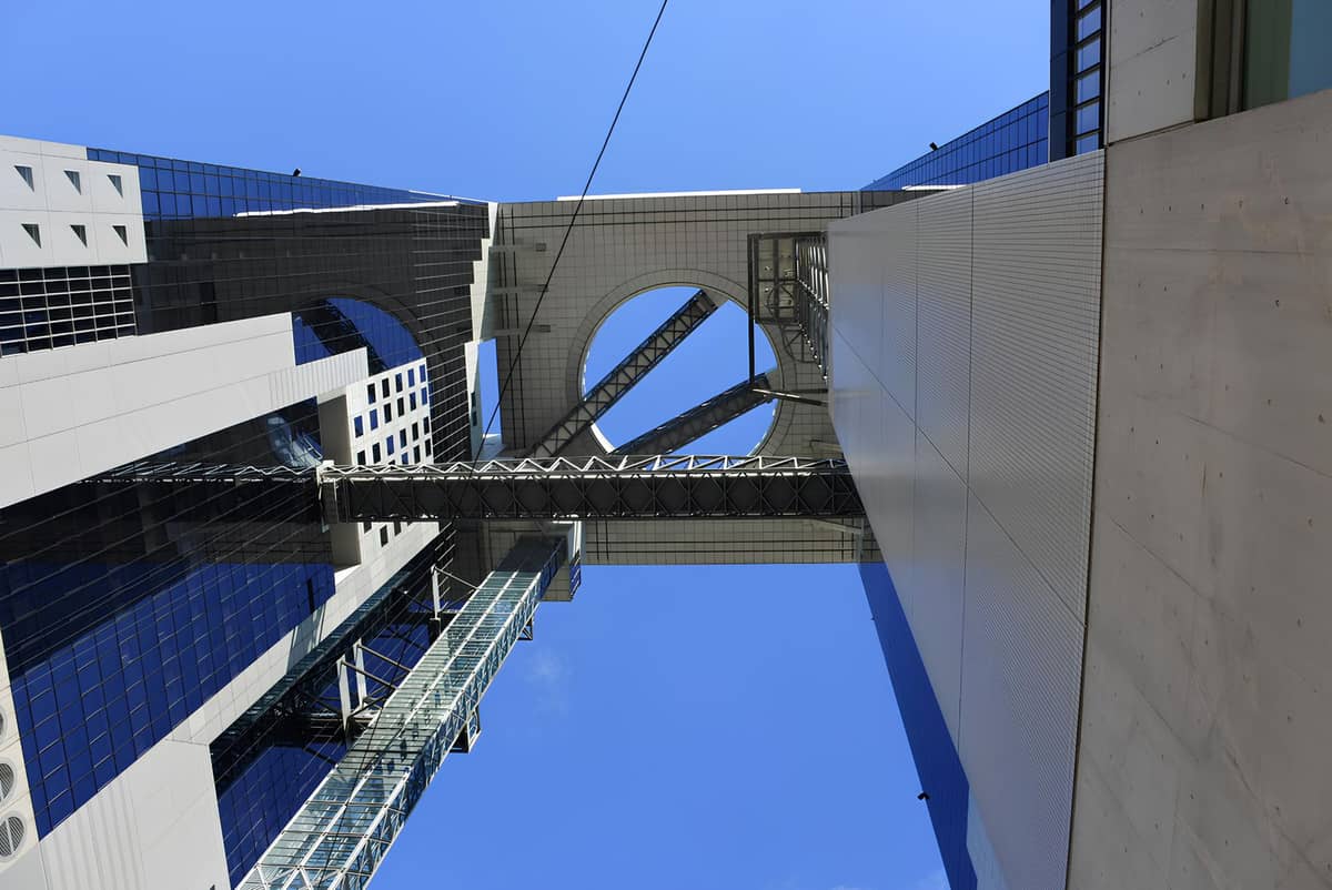 View looking straight up at the iconic Umeda Sky Building’s dramatic architecture and sky bridge set against a clear blue sky in Osaka.