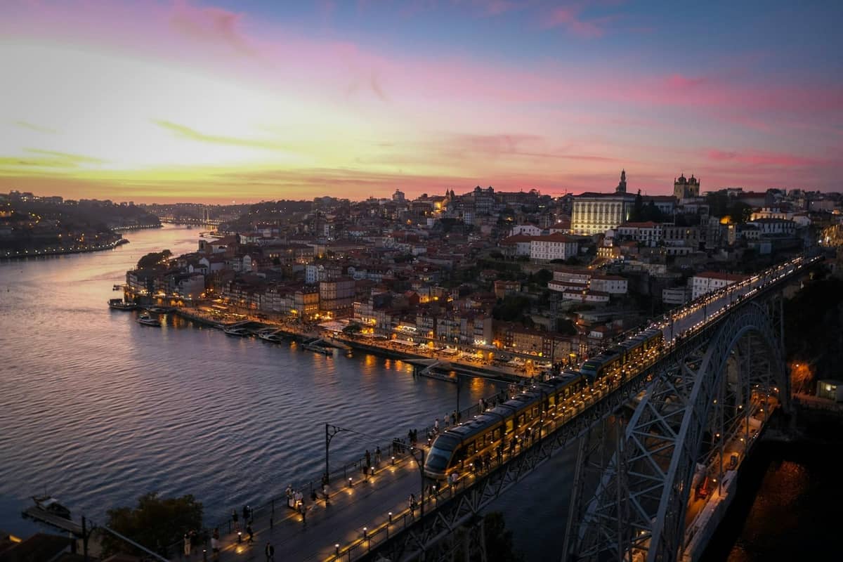 Panorama Porto o zachodzie słońca z Mostem Dom Luís I i rzeką Douro, oświetlone ulice i promenada wzdłuż kolorowych budynków miejskich.