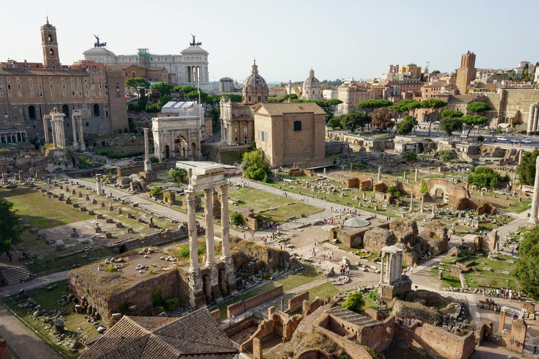 Wide view of the Roman Forum ruins with ancient columns, temples, and historic buildings in central Rome on a sunny day.