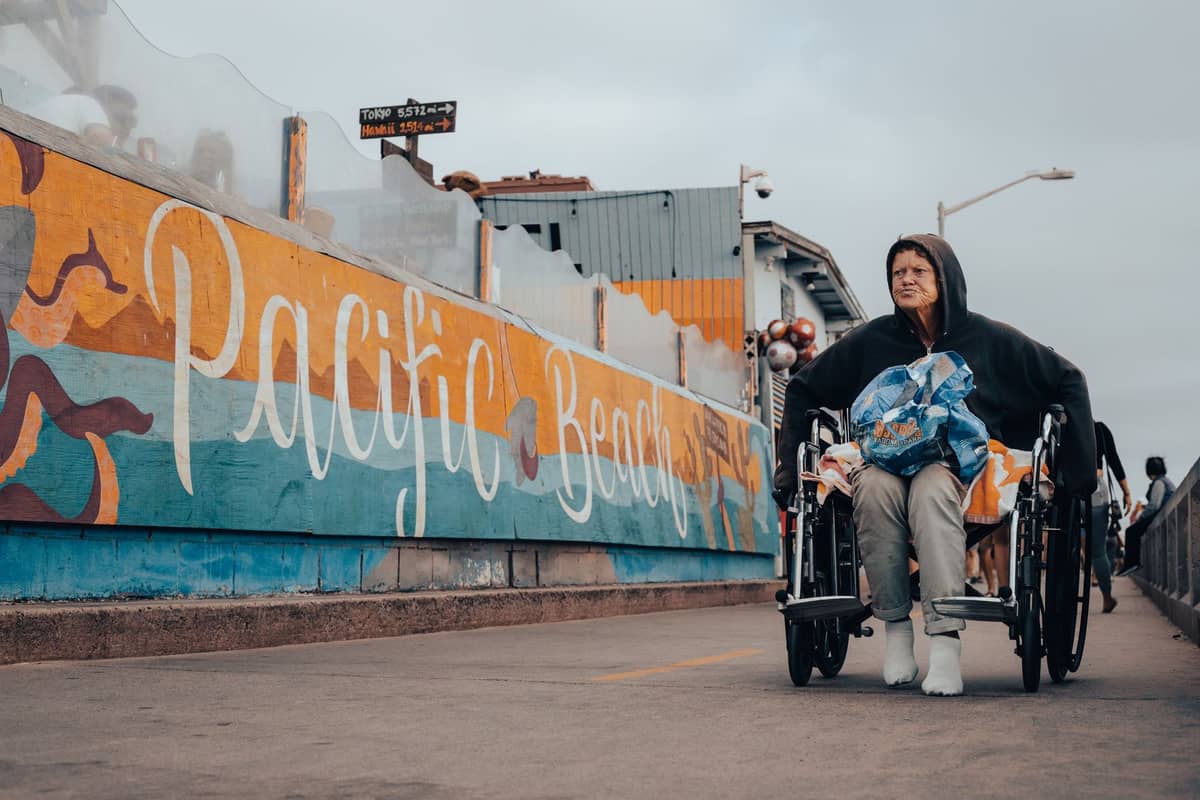 บุคคลบนรถเข็นบนทางเดินไม้ข้างจิตรกรรมฝาผนังสีสันสดใสของ Pacific Beach ใน San Diego พร้อมศิลปะข้างถนนที่มีชีวิตชีวาและบรรยากาศเมือง