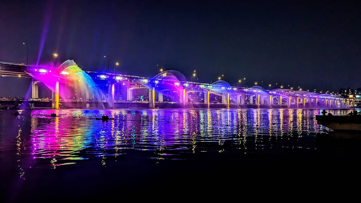 Fonte Arco-Íris da Ponte Banpo em Seul à noite, iluminada com luzes coloridas e jatos de água criando reflexos vibrantes no Rio Han.