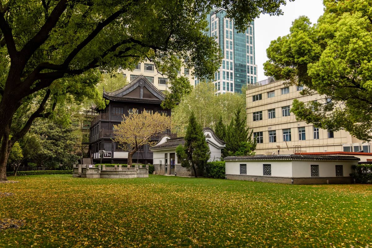 Un parc verdoyant à Shanghai avec des arbres feuillus, une architecture chinoise traditionnelle et des immeubles modernes en arrière-plan.