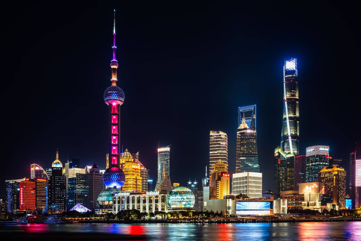 Nächtliche Ansicht von Shanghais ikonischer Skyline mit dem hell erleuchteten Oriental Pearl Tower, modernen Wolkenkratzern und dem Huangpu-Fluss im Vordergrund.