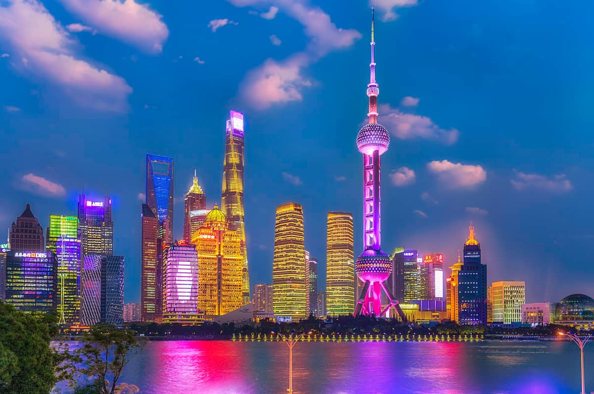 Vue nocturne de la skyline de Pudong à Shanghai depuis le bord de l'eau, avec l'Oriental Pearl Tower brillamment éclairée et les gratte-ciel modernes se reflétant dans le fleuve.