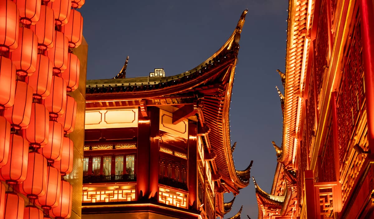 Architecture chinoise traditionnelle et lanternes rouges lumineuses dans la vieille ville de Shanghai au crépuscule, avec des toitures ornées et de riches détails décoratifs.
