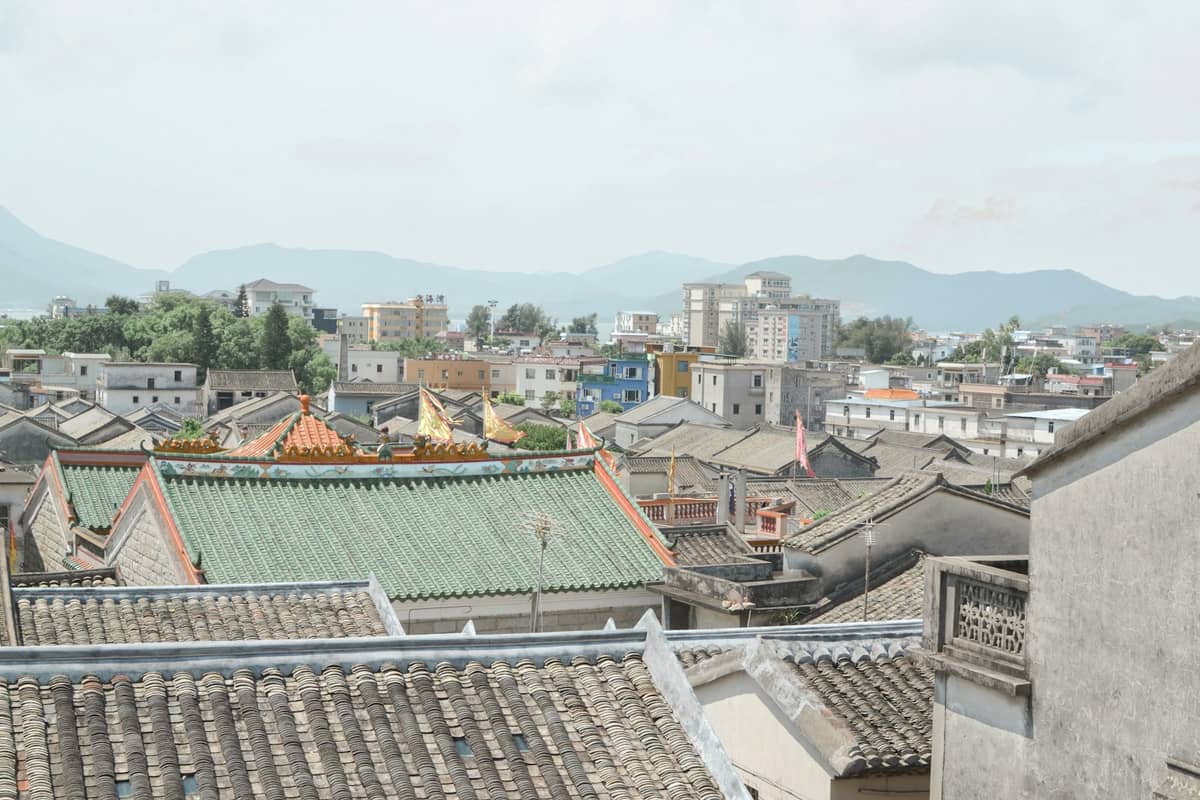 Vista do terraço de antigos edifícios com telhados e templos rodeados por uma paisagem urbana moderna e montanhas, ilustrando os bairros históricos de Shenzhen.
