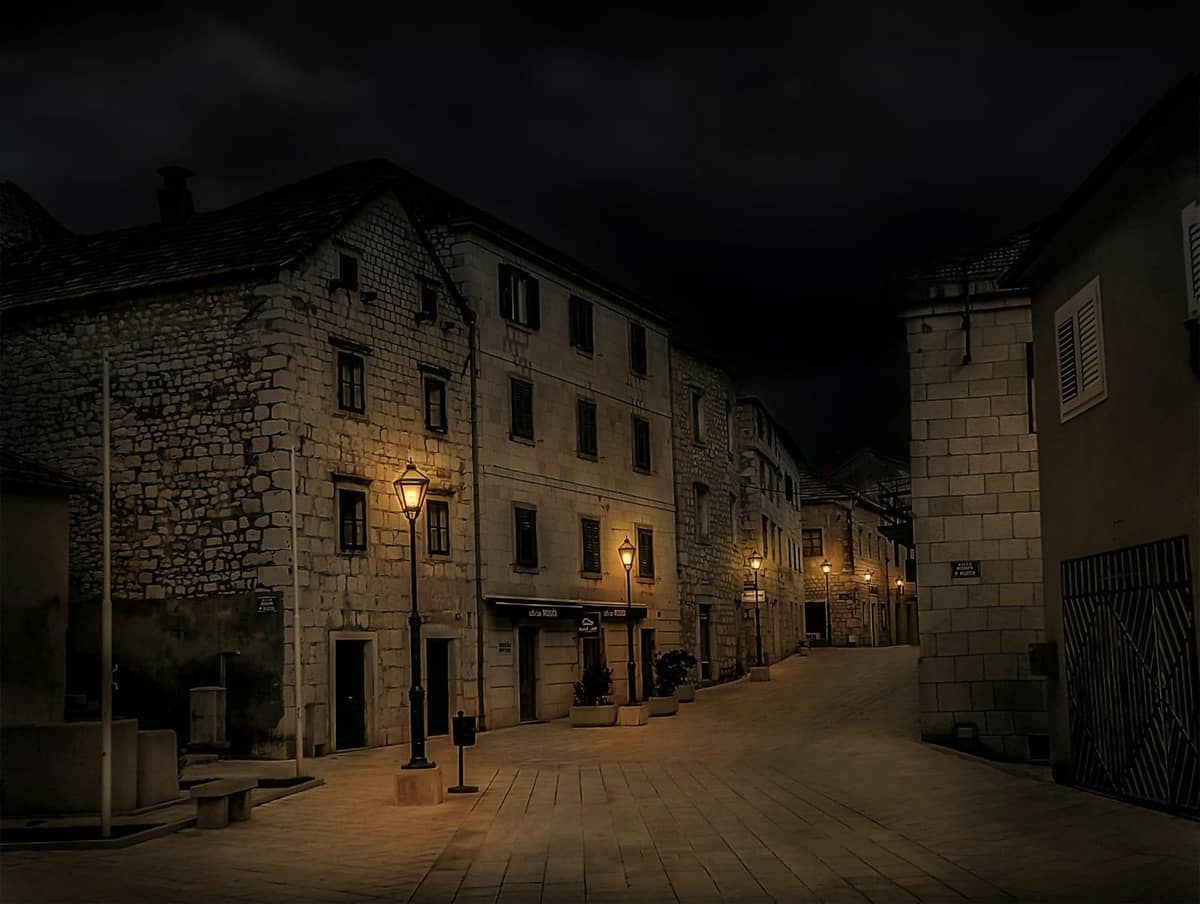 Vicolo in pietra vuoto con edifici storici a Spalato di notte, illuminato da lanterne d'epoca.