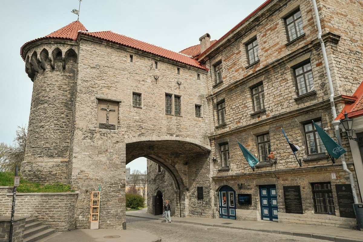 Torre-portal de pedra medieval e rua de calçada na Cidade Velha de Tallinn, com edifícios históricos e telhados vermelhos.
