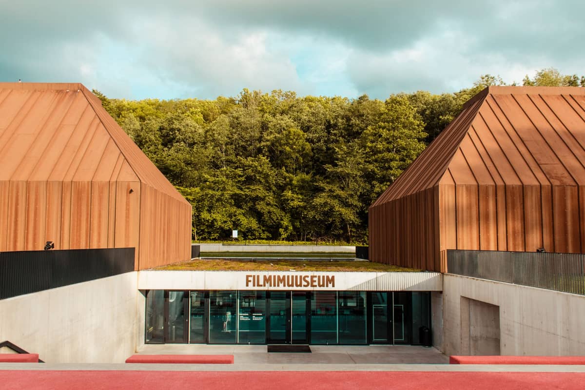 Entrada moderna do Tallinn Film Museum com edifícios de cor ferrugem distintos e vegetação ao fundo.