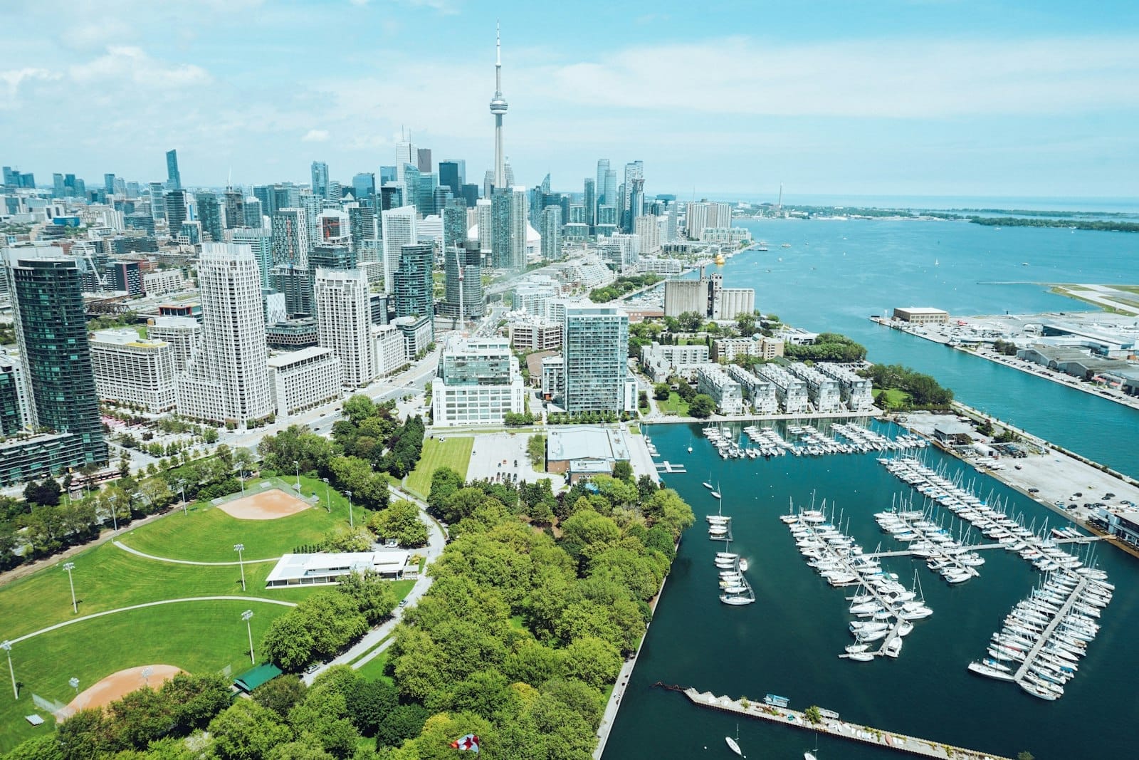 Vista aérea do skyline de Toronto com orla marítima, parques verdes, marina e CN Tower em um dia ensolarado.