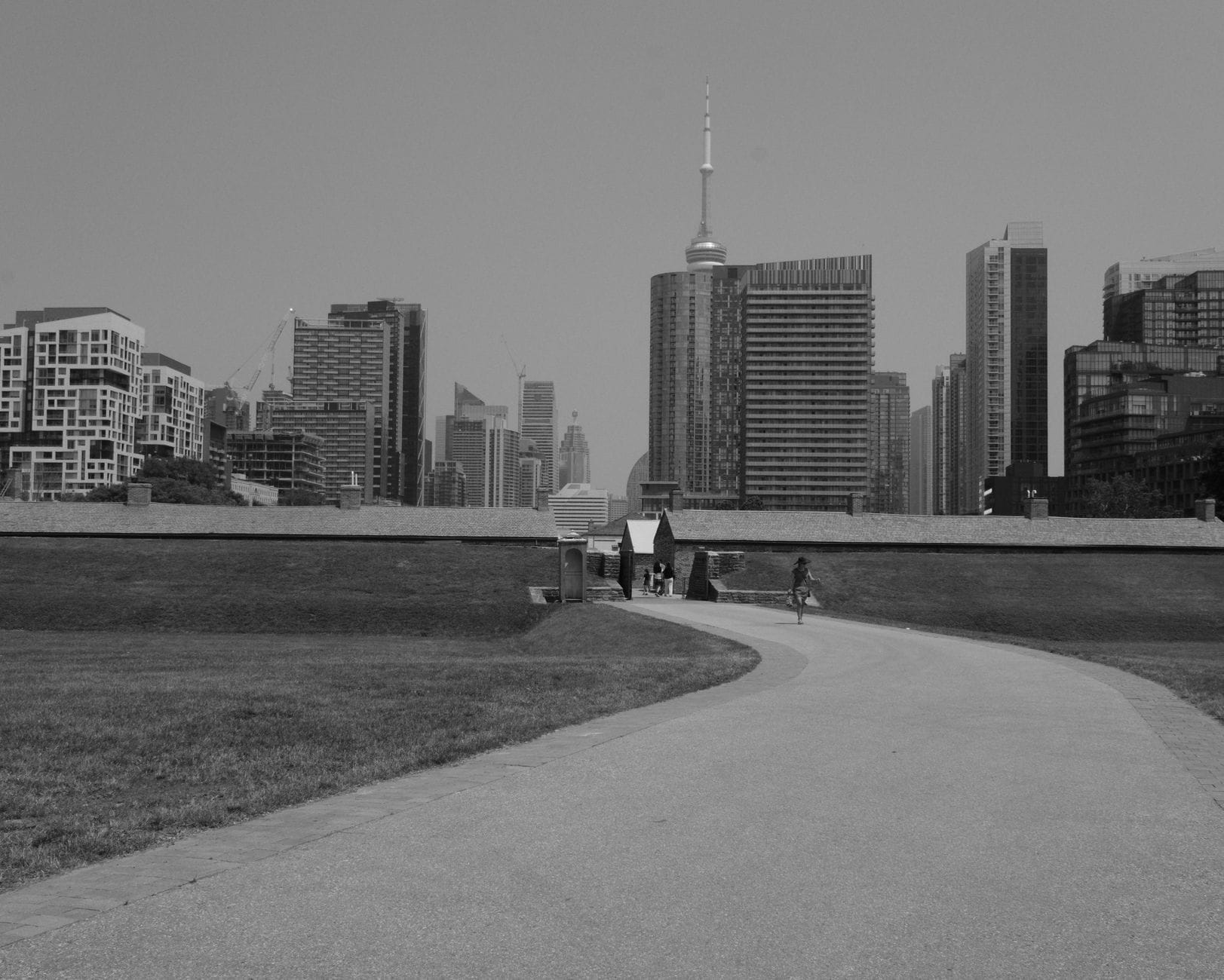 Vista de Fort York com o horizonte de Toronto e a CN Tower ao fundo, caminho que leva às históricas muralhas do forte, em preto e branco.