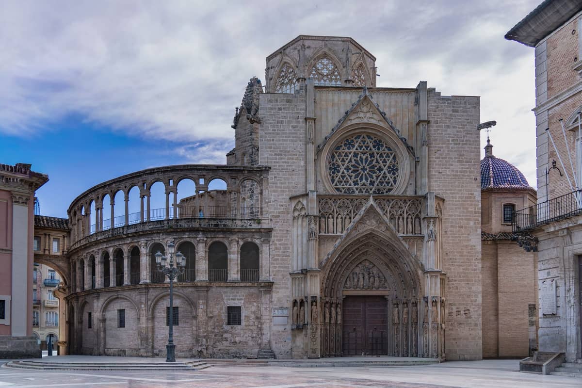 Vista grandangolare della facciata gotica della Cattedrale di Valencia con rosone e gli edifici storici circostanti sotto un cielo azzurro.