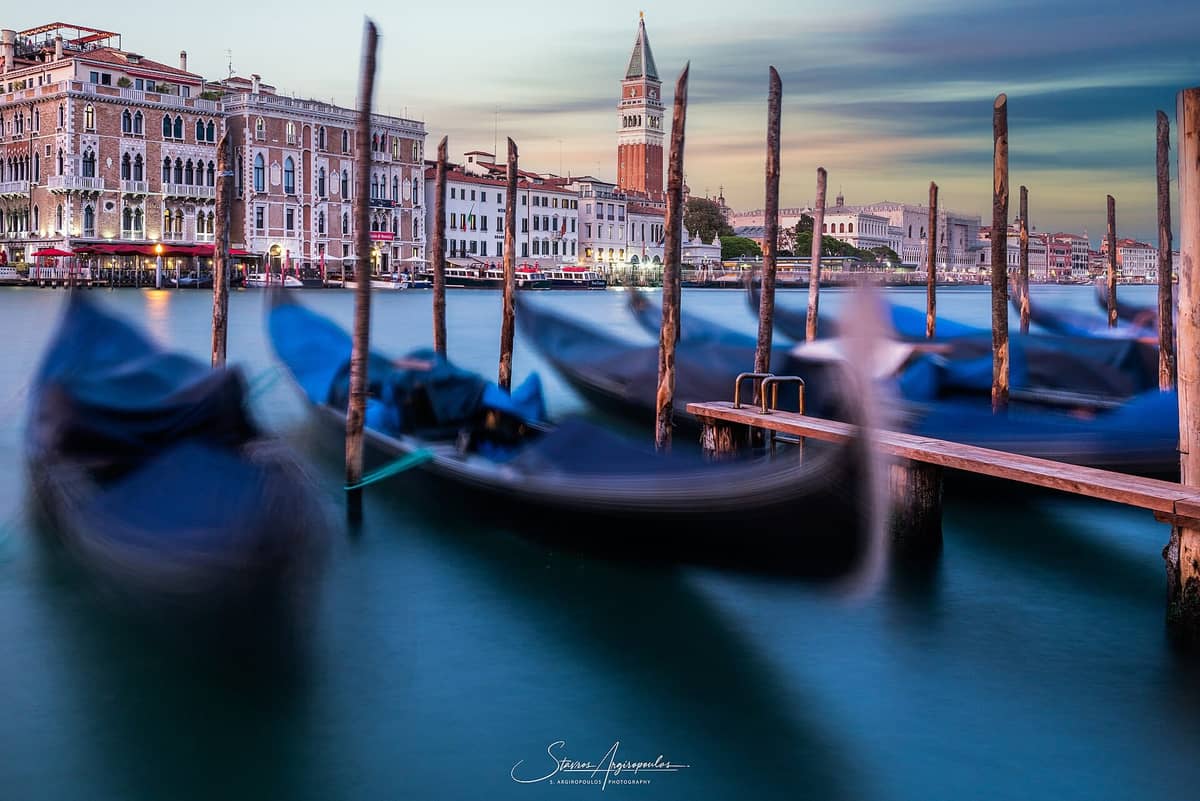 Sonnenuntergang über dem Canal Grande in Venedig mit festgemachten Gondeln, dem Campanile di San Marco, dem Palazzo Ducale und historischen venezianischen Gebäuden im Hintergrund.