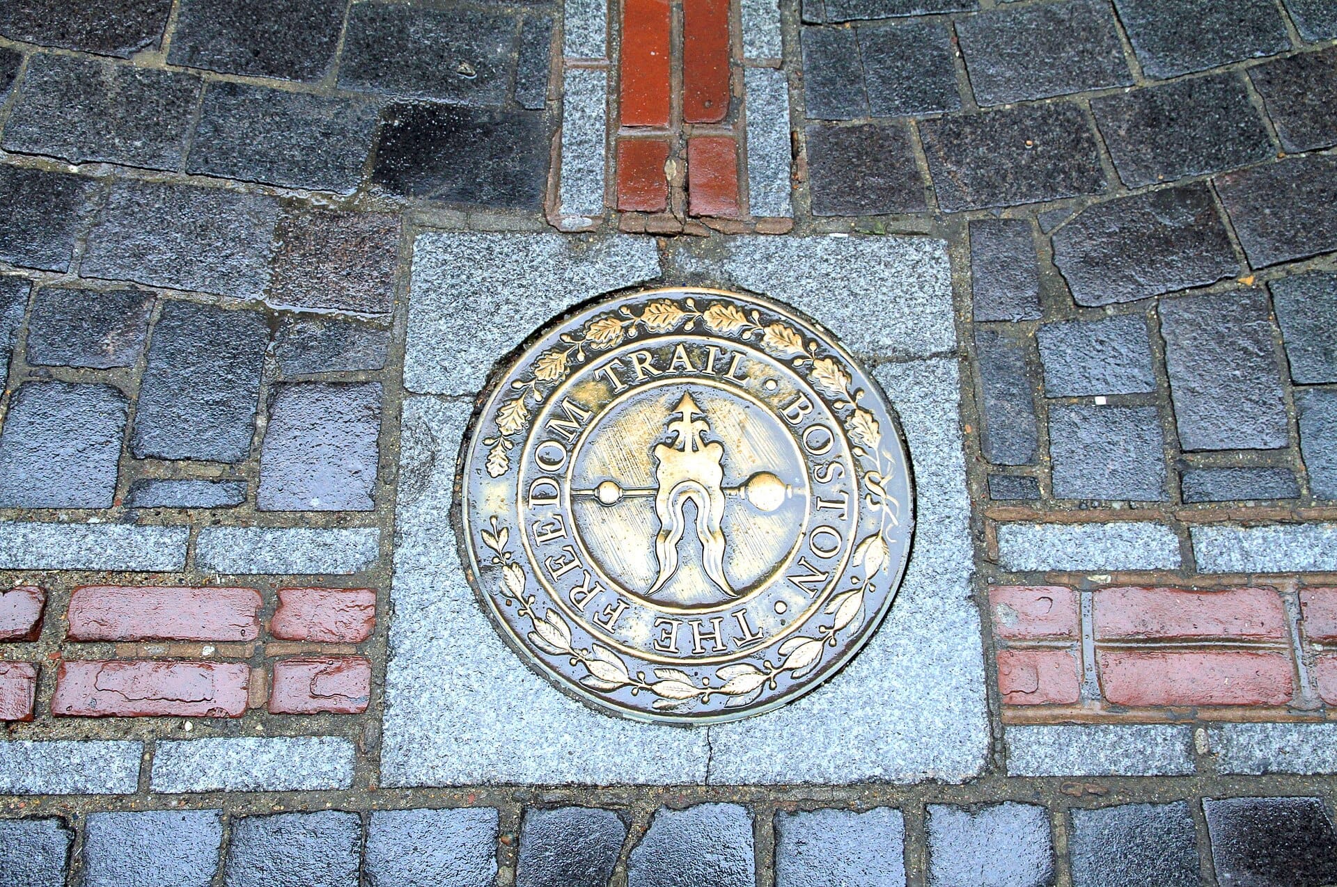 Primo piano del medaglione del Freedom Trail incastonato in un marciapiede acciottolato a Boston, con mattoni rossi e pietre grigie visibili intorno.