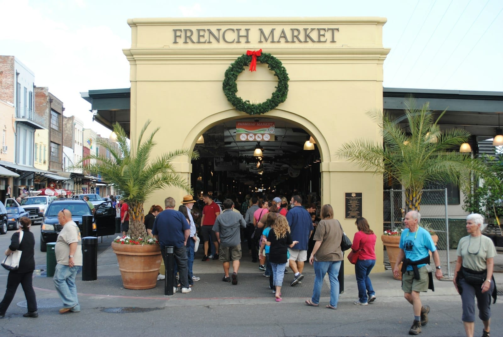 Ingresso al French Market di New Orleans con una corona festiva, palme e folle di persone che camminano fuori e all'interno.