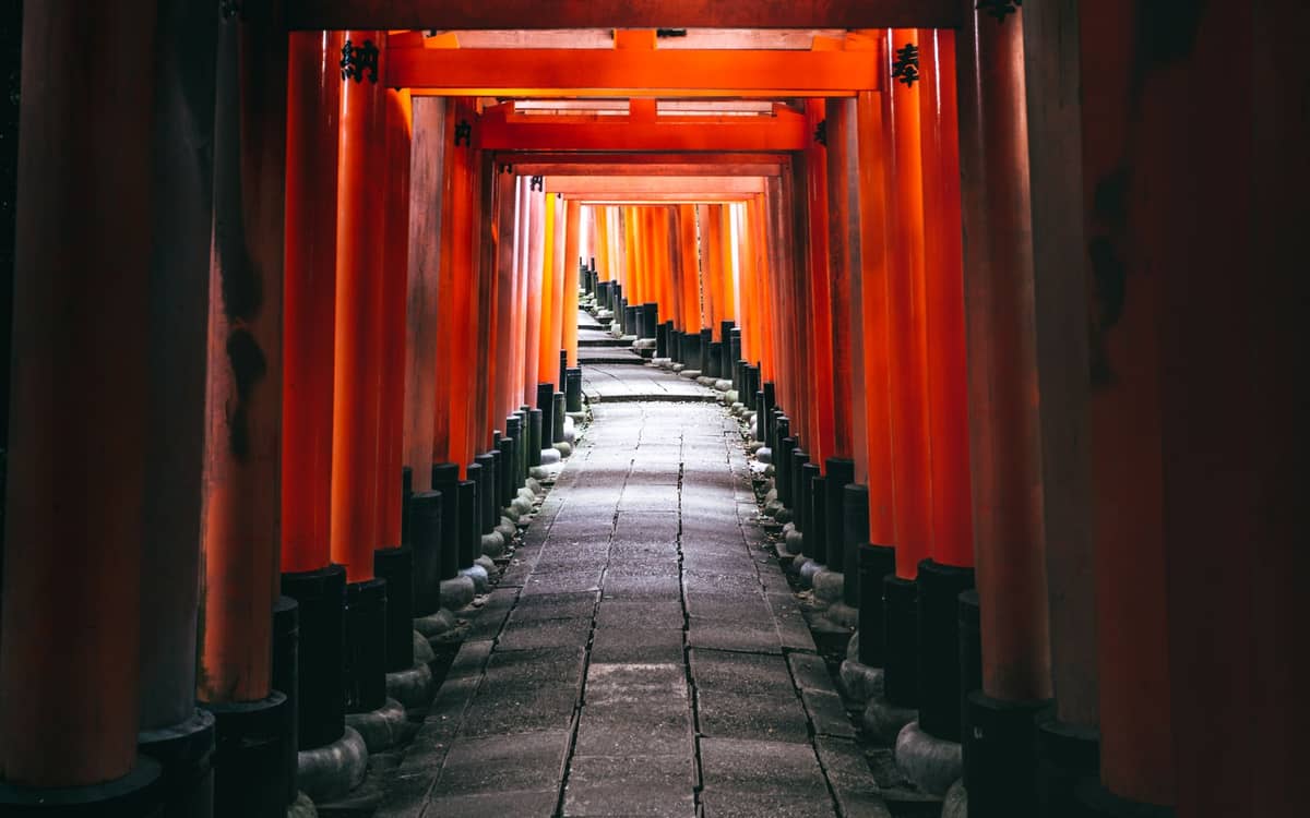 Long, continuous tunnel of closely spaced orange torii gates winding uphill along the Fushimi Inari trail in Kyoto, Japan.
