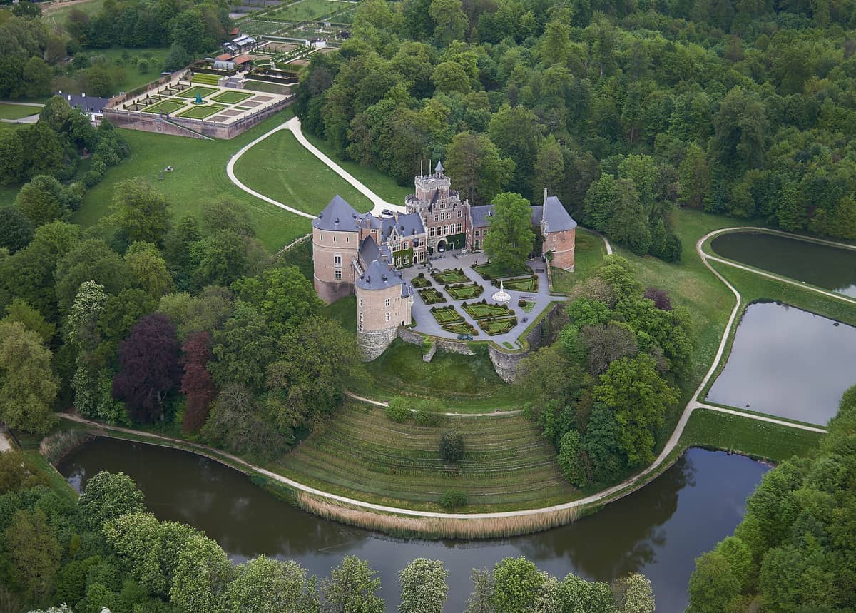 Vista aérea do Castelo de Gaasbeek rodeado por árvores verdes exuberantes, jardins formais e lagos com reflexos na campanha flamenga perto de Bruxelas.