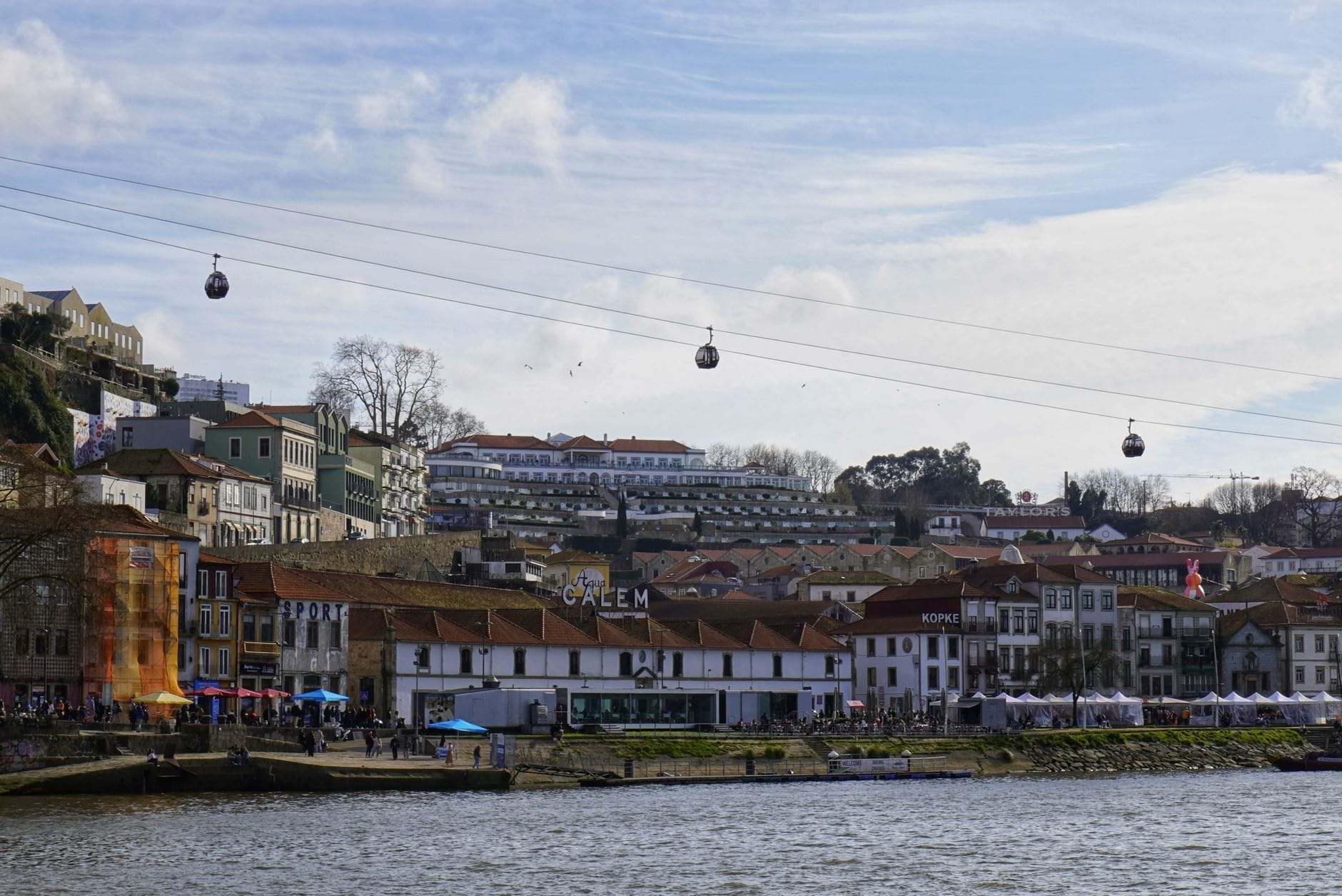 Le cabine della funivia scivolano sopra il lungofiume di Vila Nova de Gaia verso il Ponte Dom Luís I, con gli edifici storici lungo il Douro sotto un cielo azzurro.