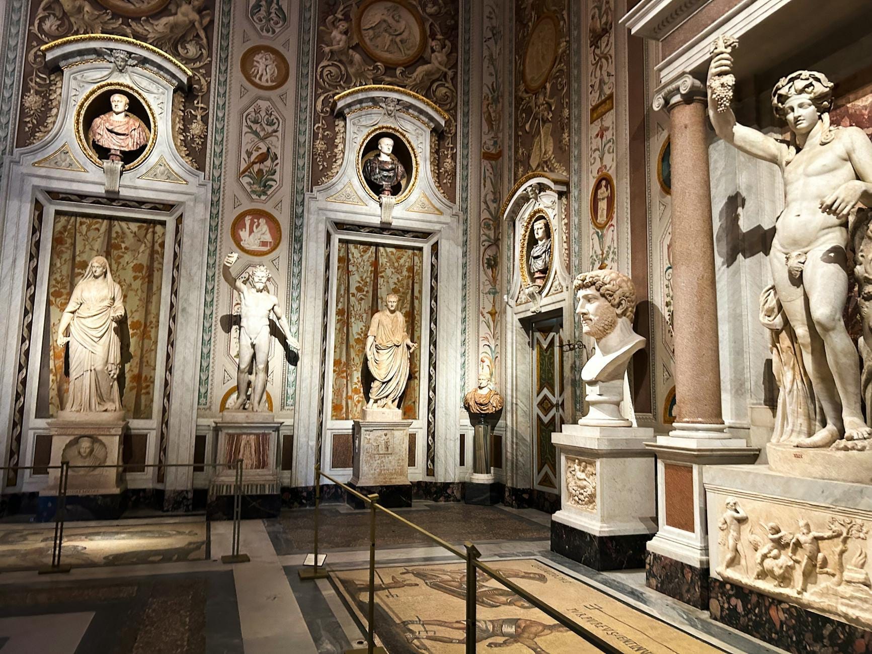 Lavishly decorated gallery hall inside Galleria Borghese with classical sculptures, marble floors, ornate walls, and dramatic Baroque details under soft indoor lighting.
