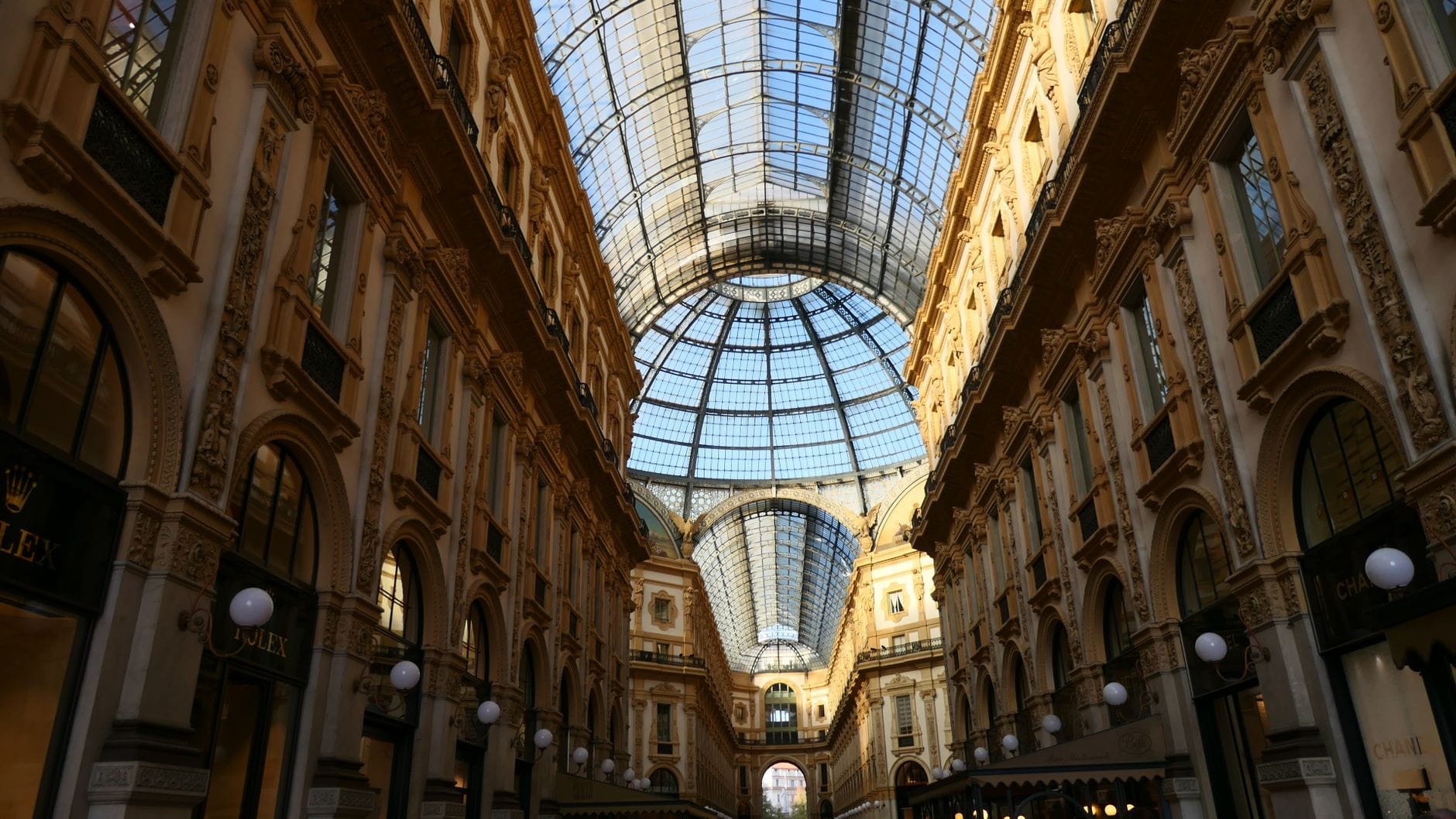 Vista ampia della sontuosa cupola di vetro della Galleria Vittorio Emanuele II con la sua elegante architettura ottocentesca, la luce solare che illumina l'ampia galleria e le vetrine dei negozi di lusso a Milano.
