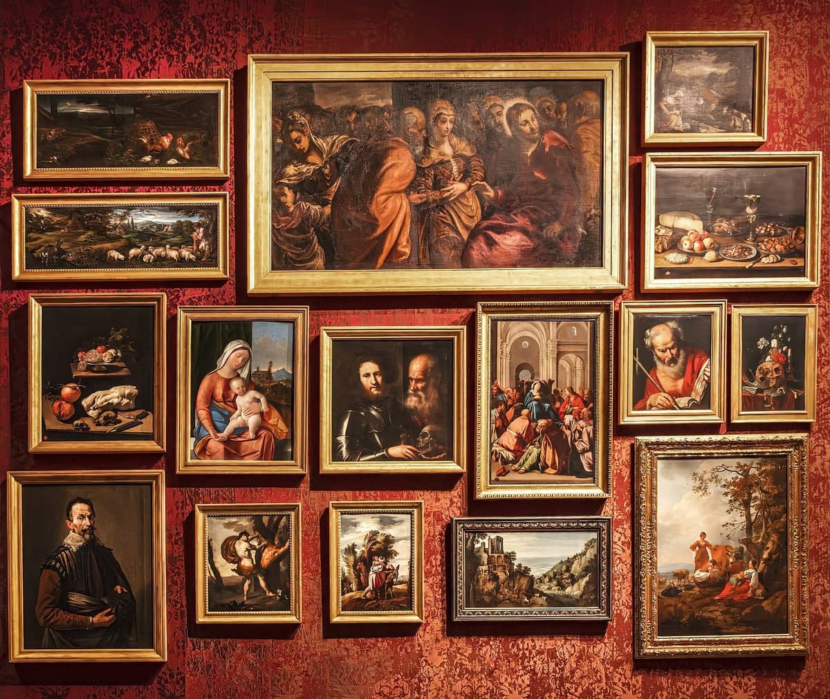 Galeriewand in den Gallerie dell'Accademia mit gerahmten venezianischen Gemälden auf reichem rotem Mustertapete unter warmem Licht.