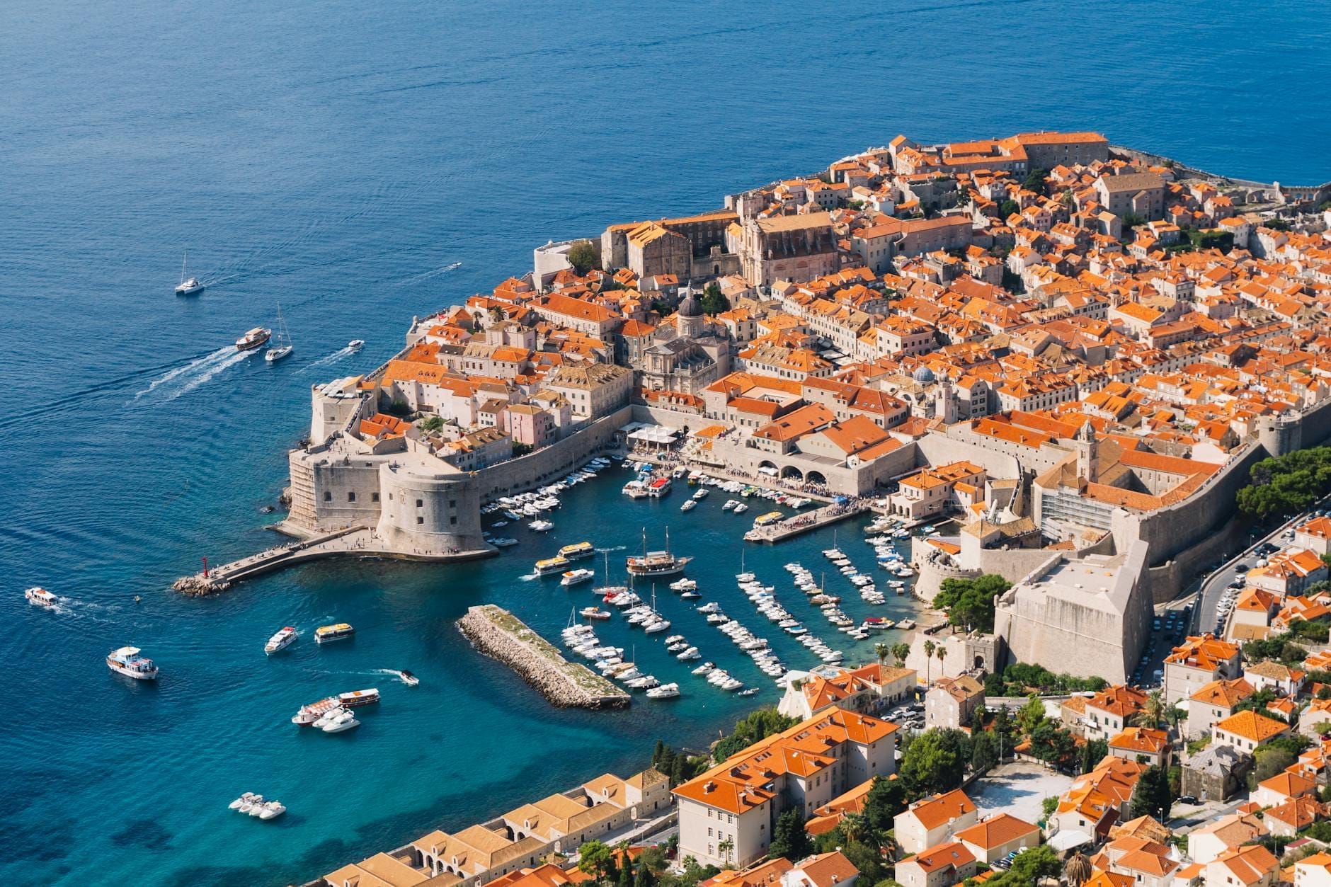 Una impresionante vista aérea de las murallas fortificadas y el puerto de la Ciudad Vieja de Dubrovnik, con barcos amarrados junto al reluciente mar Adriático, escenario real del Desembarco del Rey.