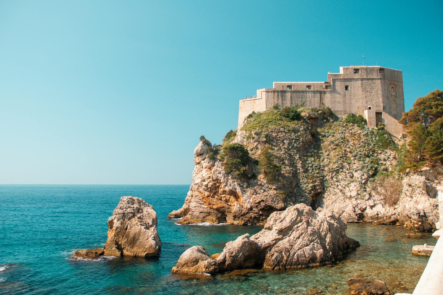 Fort Lovrijenac encaramado en un acantilado rocoso sobre el azul cristalino del mar Adriático bajo un cielo luminoso y soleado en Dubrovnik, Croacia.