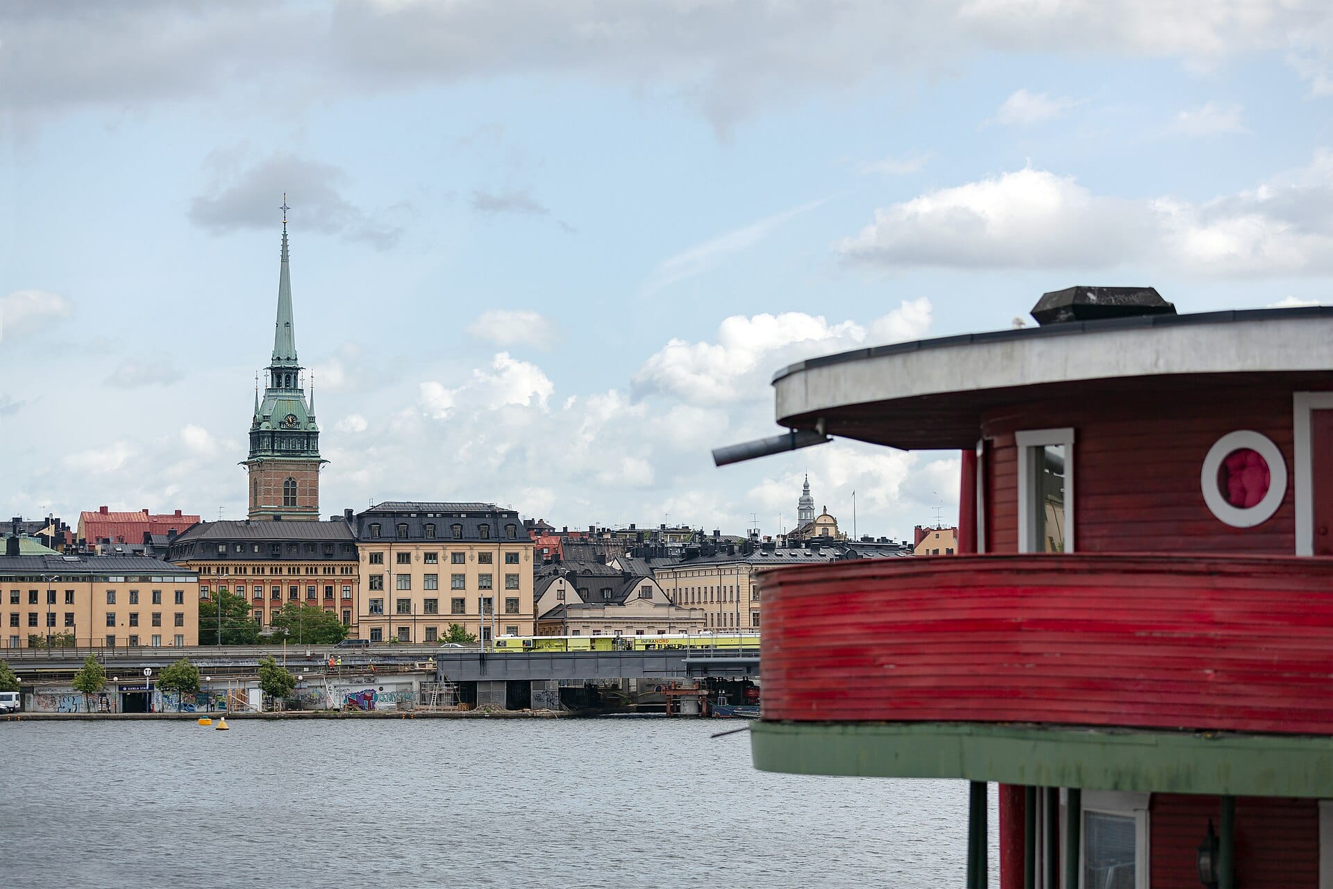 วิวมองข้ามน้ำไปยังยอดแหลมของ Tyska Kyrkan (โบสถ์เยอรมัน) โผล่เหนือตึกเก่าใน Gamla Stan เมืองสตอกโฮล์ม ในวันฟ้าครึ้ม