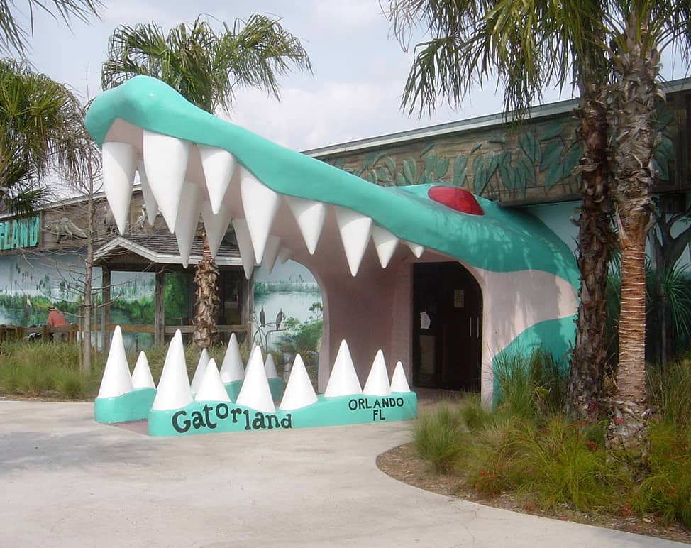Eingang zu Gatorland Orlando mit einer riesigen Alligatormaul-Struktur mit weißen Zähnen, umgeben von Palmen und gemalten Tierwelt-Wandgemälden.