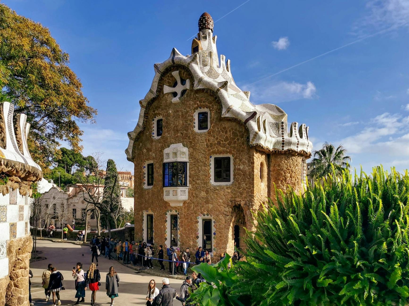 Exterior of the Gaudí House Museum in Park Güell with visitors and distinctive whimsical architecture on a sunny day.