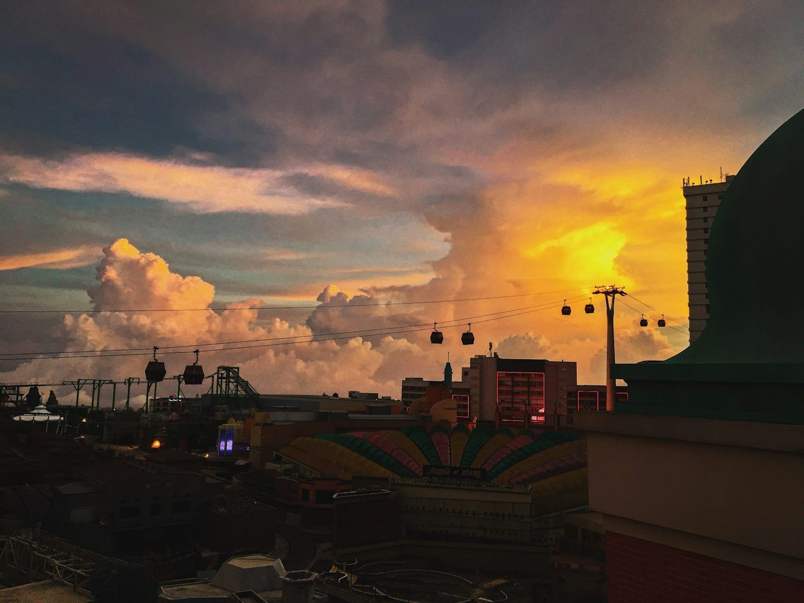 Warm, golden sunset bathes Genting Highlands in soft light, highlighting dramatic clouds and silhouetted cable cars gliding above the hilltop resort.