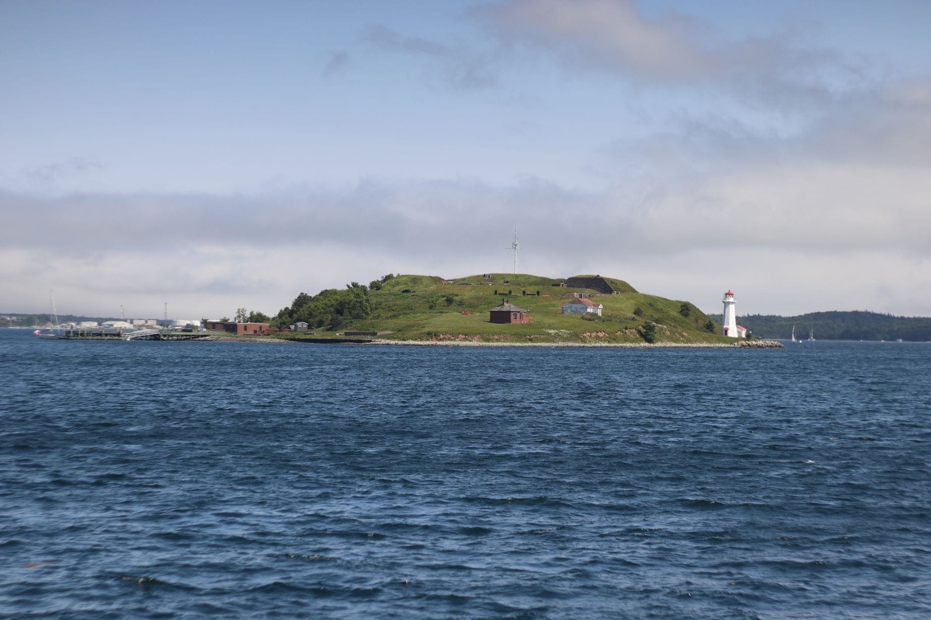 Vista ampia di Georges Island nel porto di Boston: paesaggio erboso, edifici storici del forte, acque blu tutt'intorno e cielo limpido in pieno giorno.