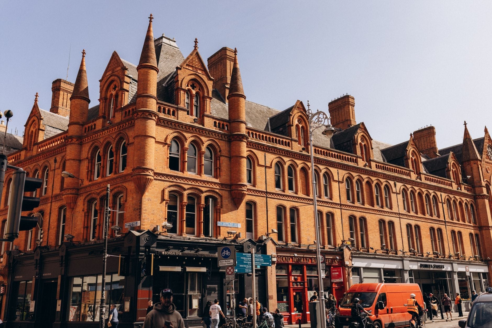 Vista grandangolare dell'esterno di George's Street Arcade, con la storica facciata vittoriana in mattoni rossi, gli archi a punta e il viavai della strada animata davanti all'ingresso.