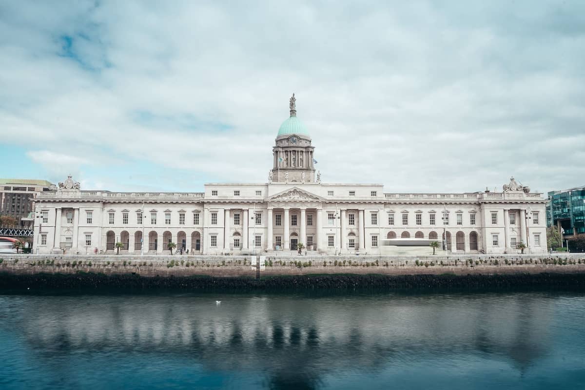 Vollständige Flussuferansicht des georgianischen Custom House in Dublin mit seiner zentralen Kupferkuppel, klassischer Fassade und klarem, im Wasser gespiegeltem Himmel.