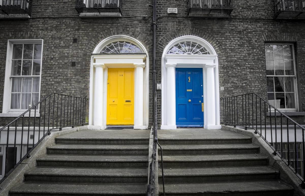 Zwei klassische georgianische Eingangstüren, eine gelbe und eine blaue, mit Fächeroberlichten und Steinstufen auf einer Backsteintetrasse in Dublin.