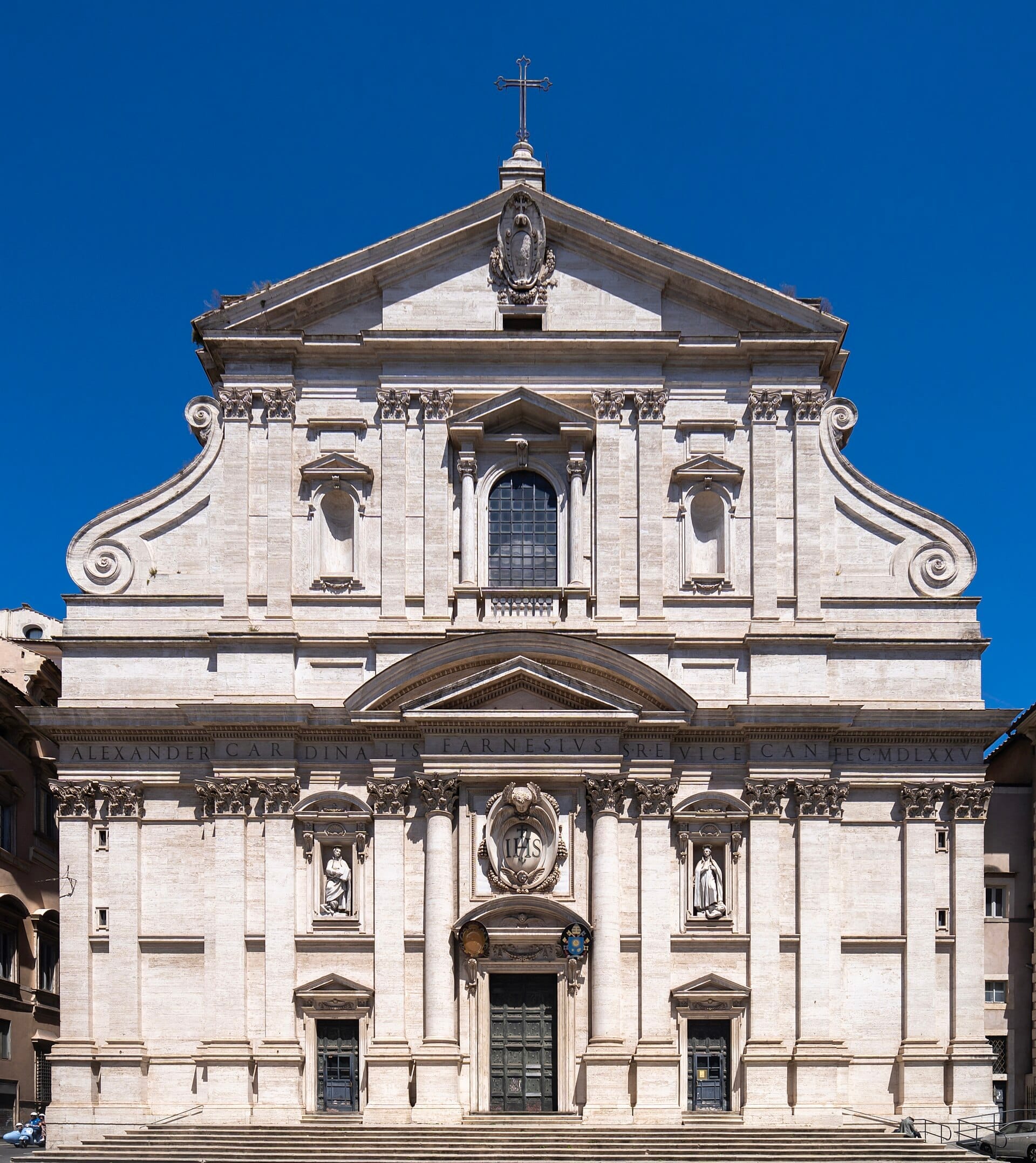 The impressive stone facade of the Gesù Church in Rome, featuring ornate Baroque architecture against a clear blue sky.