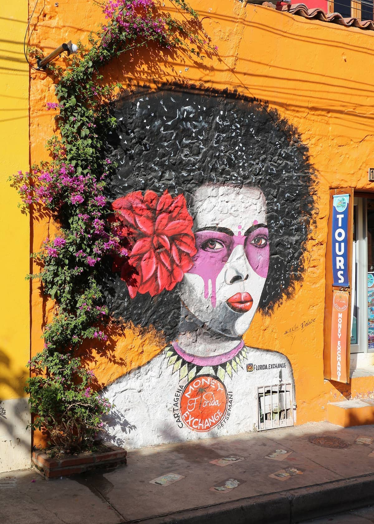Colorful mural of a woman's face with an afro and a red flower, painted on a vibrant orange wall in Getsemaní, Cartagena.