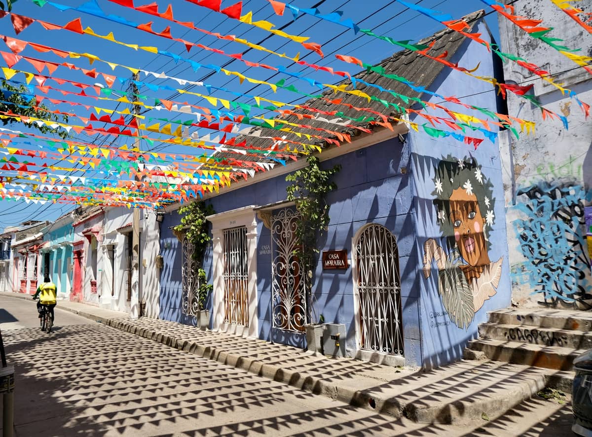 A vibrant street in Getsemaní, Cartagena, lined with colorful murals and shaded by festive hanging flags, typical of the neighborhood’s lively atmosphere.